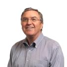 Smiling middle-aged man in a button-up shirt with glasses against a white background.