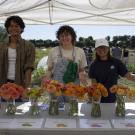A group of three students standing behind a table displaying zinnias in vases
